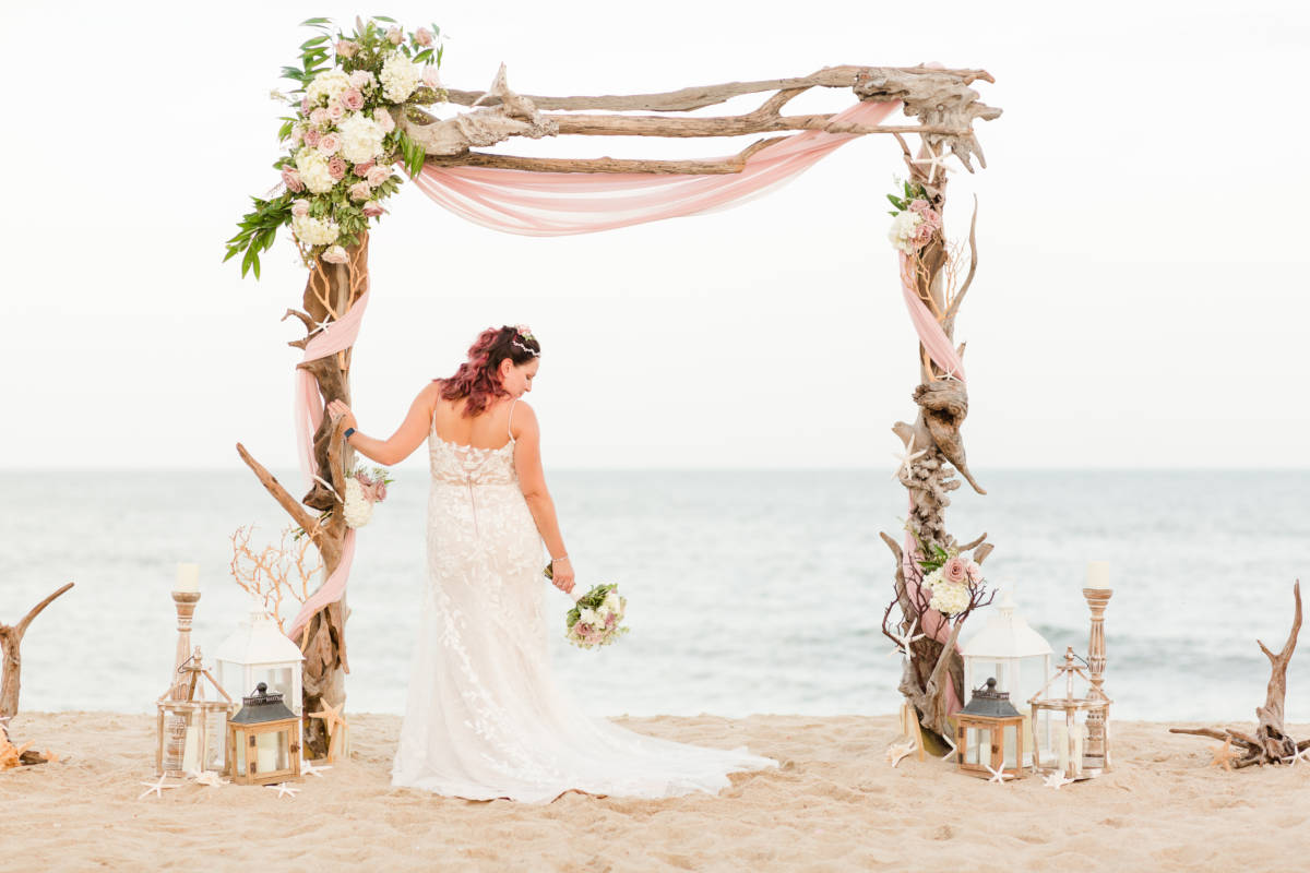 Outer Banks Wedding Arch ceremony set up with Bride leaning against arch and holding bouquet